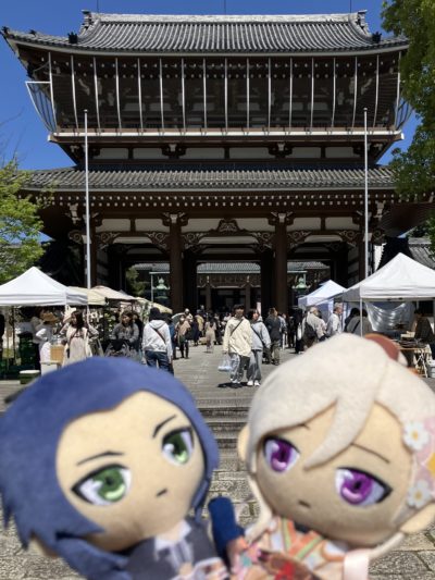 平日なのにめっちゃたくさんの東別院。奥に東別院の山門、その前にはマルシェでのおかいものを楽しむ人々であふれている。そしてそれを見て驚く帝釈天＆梵天ぬいぐるみ。